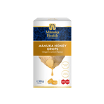 A box of Mânuka Health Mânuka Honey Drops (Ginger & Lemon Flavour) on a solid white background. The packaging is white with a dark blue band at the top, a gold banner, and an illustration of honey dripping from a piece of ginger root.