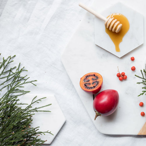 Honeycomb with honey drizzled on a white marble surface with red fruits and green leaves.