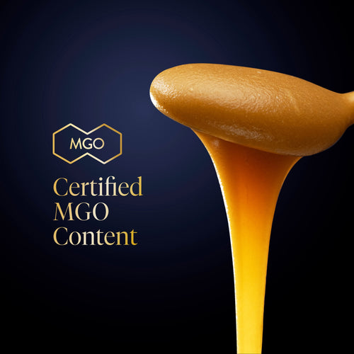 A thick, glossy golden-brown honey-like substance drips from a spoon against a dark navy background, with the text 'MGO Certified MGO Content' and an MGO logo on the left.