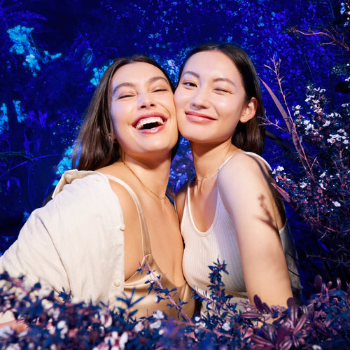 Two women laughing together with a blue floral background.