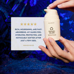 A person's hands hold a bottle of Manuka Health Pro Vitality Moisturizing Hand Cream next to a white card with a verified buyer review, set against a dark blue, textured background.